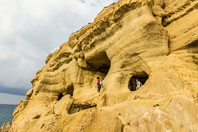 People walking on rock formation against sky