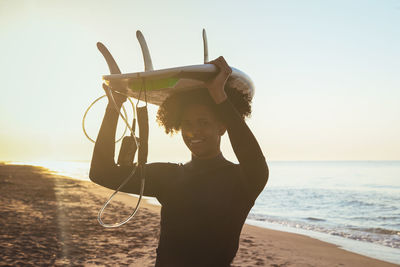 Woman with arms raised standing on beach against sky