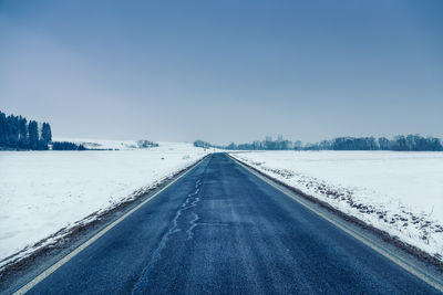 Road amidst snow covered landscape against clear sky