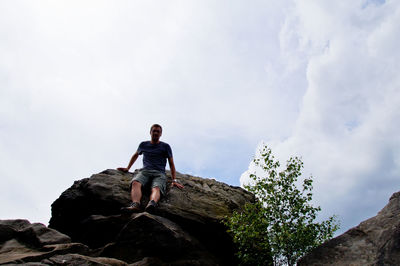 Low angle view of young man standing on cliff against sky