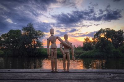Wooden figurines by lake during sunset