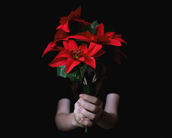 Woman holding red flowers in front of face while standing against black background