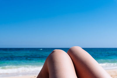 Midsection of woman relaxing at beach against clear blue sky on sunny day