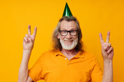 Portrait of senior man gesturing against yellow background