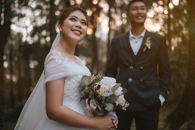 Smiling bridegroom looking away while standing outdoors