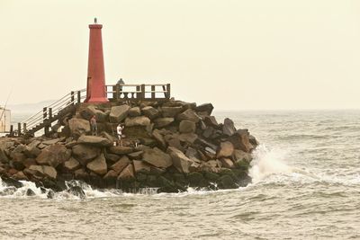 Lighthouse on rocks by sea against clear sky