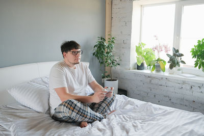 Young woman using digital tablet while sitting on bed at home