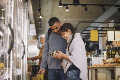 Smiling girl analyzing jars while standing by father at grocery store