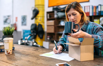 Blonde woman entrepreneur checking new merchandise received by courier to sell in her local store