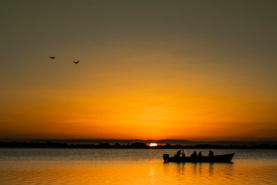 Silhouette birds flying over sea against orange sky