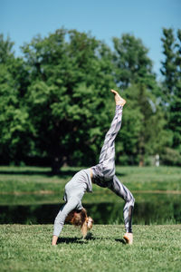 Full length of young woman exercising by pond on field