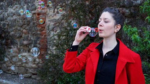 Young woman blowing bubbles against wall