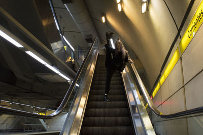 Low angle view of woman standing on one leg at escalator in subway station