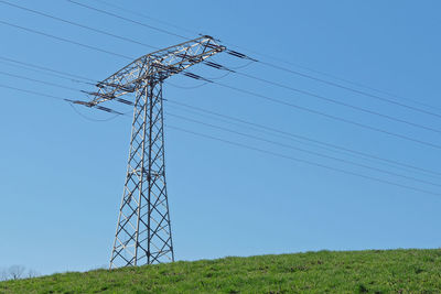 Low angle view of electricity pylon on field against clear sky