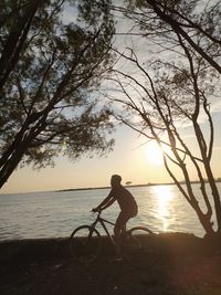 Silhouette boy on bicycle at beach against sky during sunset