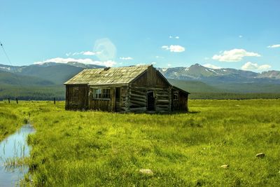 Wooden rustic house on grassy field against distant mountains