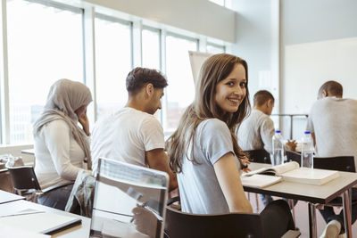 Portrait of smiling student sitting with friends in classroom at high school