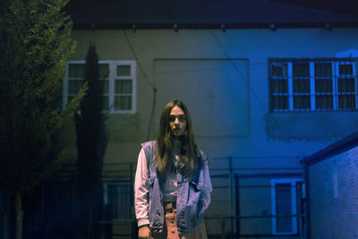 Portrait of woman standing against building in city at night