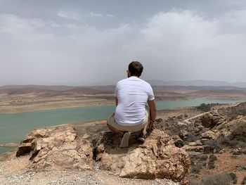 Rear view of man sitting on landscape against sky