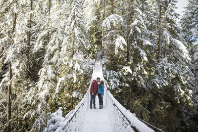 Couple kissing while standing on footbridge amidst trees in forest at lynn canyon park during winter