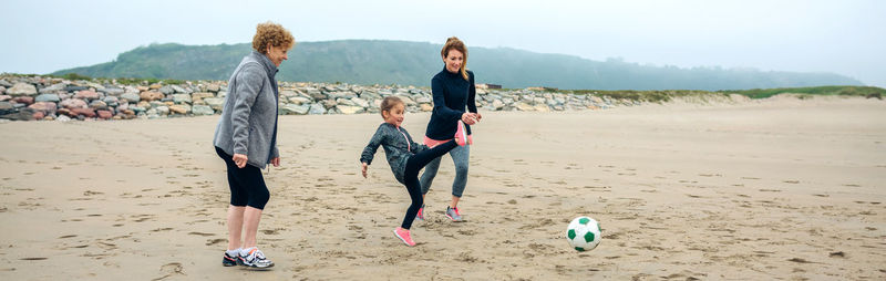 Panoramic view of family playing soccer at beach against sky