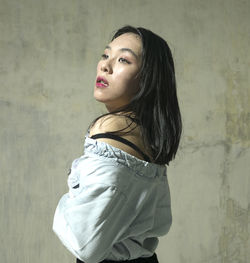 Side view of a young woman looking away against wall