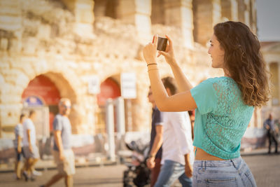 Smiling young woman photographing in city