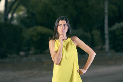 Thoughtful woman standing against trees on road