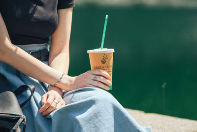 Midsection of woman holding drink while sitting outdoors