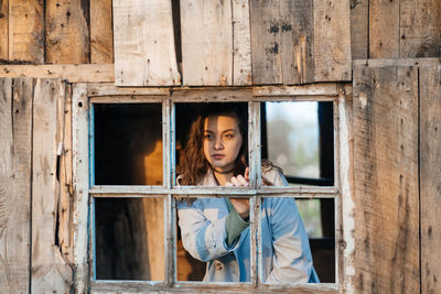 Girl looks out the window from an old wooden house, sunlight