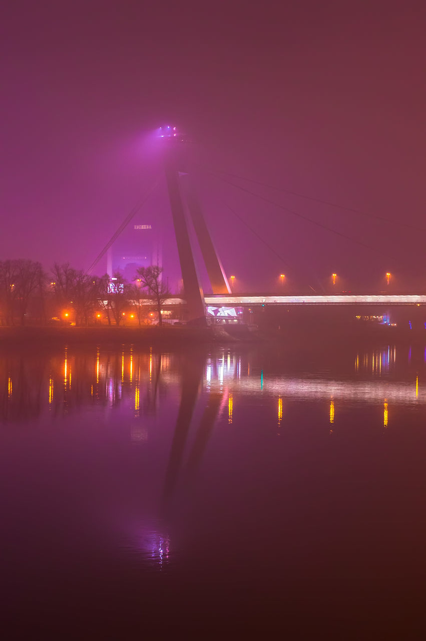 ILLUMINATED BRIDGE OVER RIVER AGAINST SKY IN CITY