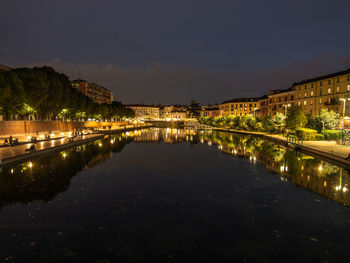 Illuminated buildings by river against sky at night