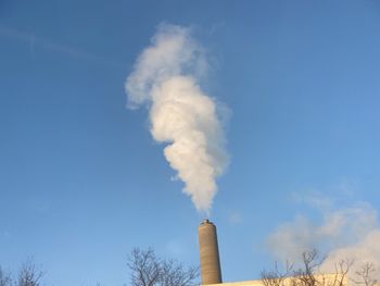 Low angle view of smoke stacks against clear blue sky