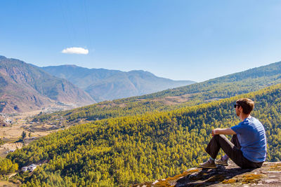 Woman sitting on mountain against sky