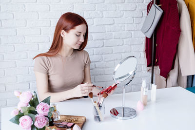 Woman holding make-up brushes and making up with cosmetics set at home