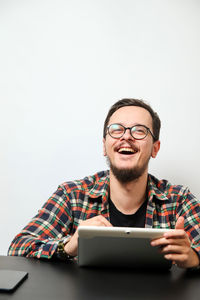 Portrait of young man using mobile phone while standing against white background