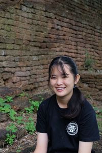 Portrait of young woman with braces smiling against brick wall