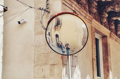 Reflection of woman photographing while standing by man against built structure in city