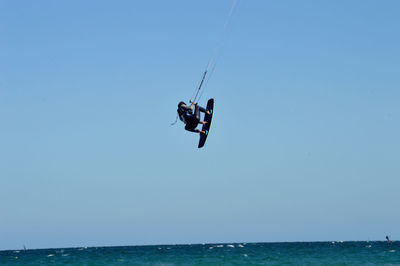 Rear view of man kiteboarding in sea against clear sky
