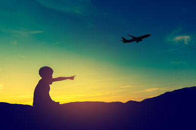 Silhouette boy gesturing while air plane flying against sky