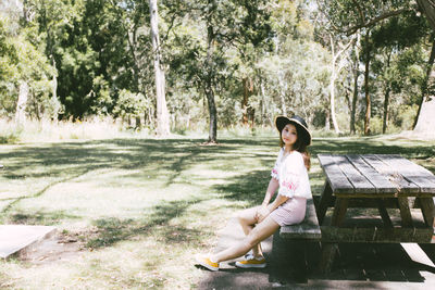 Full length portrait of mid adult woman sitting on picnic table in park