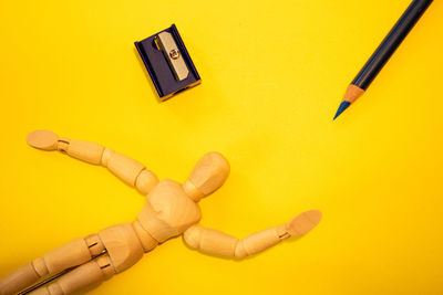 Close-up of figurine with pencil and sharpener on yellow background