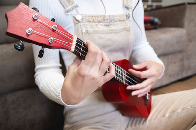 Close-up, ukulele in female hands, hipster learns to play a musical instrument at home, sitting on