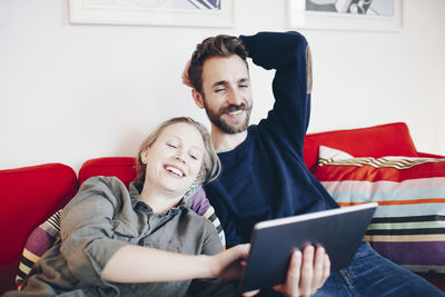 Happy of couple looking at digital tablet while relaxing on sofa in living room