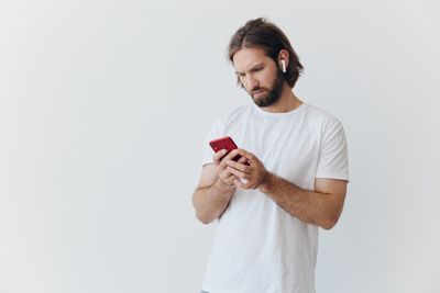 Young man using mobile phone while standing against white background