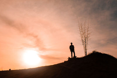 Silhouette man standing on field against sky during sunset