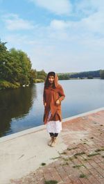 Young woman standing by lake against sky