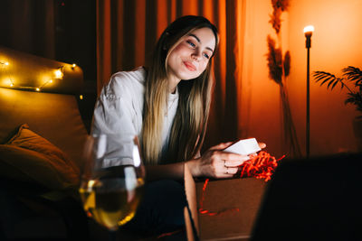 Portrait of smiling young woman sitting in illuminated room