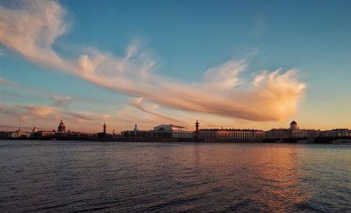 Scenic view of lake by silhouette buildings against sky during sunset