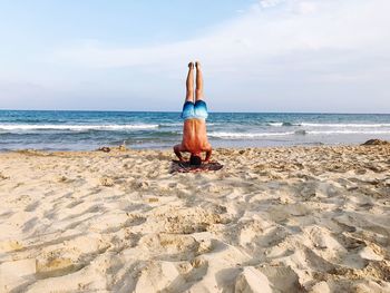 Rear view of shirtless man doing handstand on sandy beach